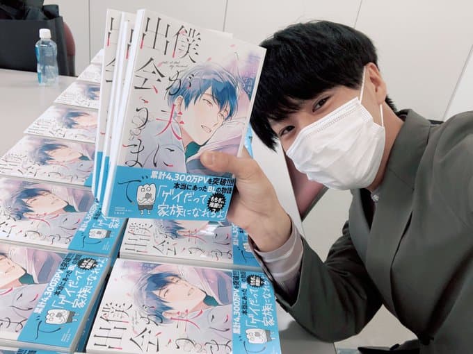 Foto dell'attivista Nanasaki che posa con un lotto del manga Boku ga otto ni deau made.